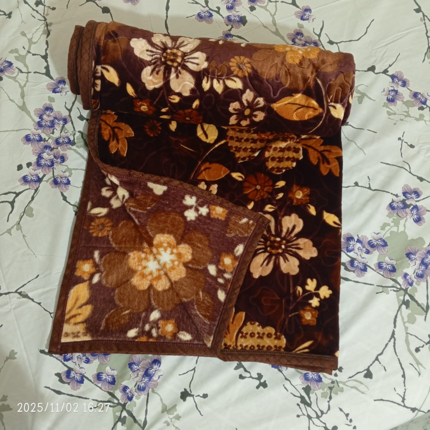 Brown floral fleece blanket on a white sheet with blue flower print