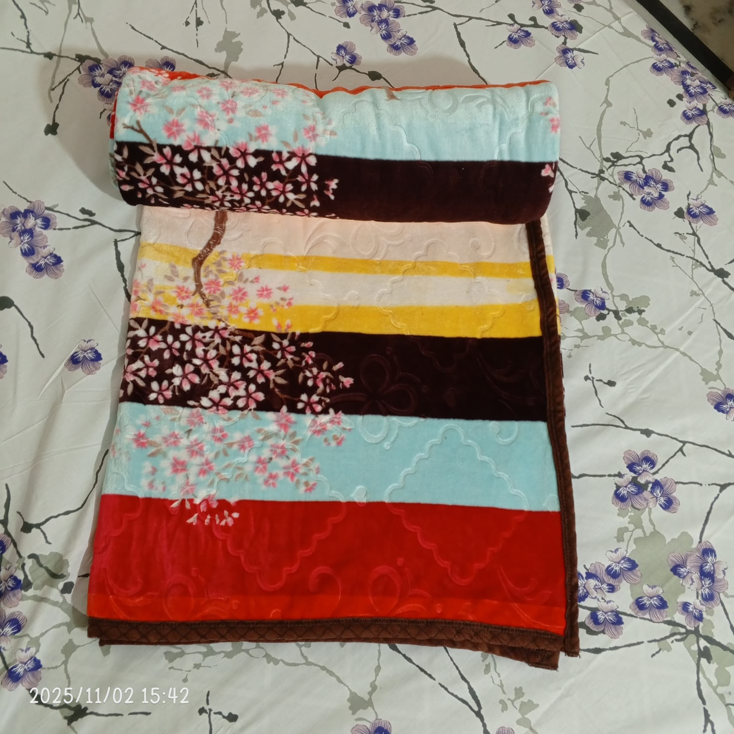 Folded floral striped blanket on a bed with purple blossom bedsheet