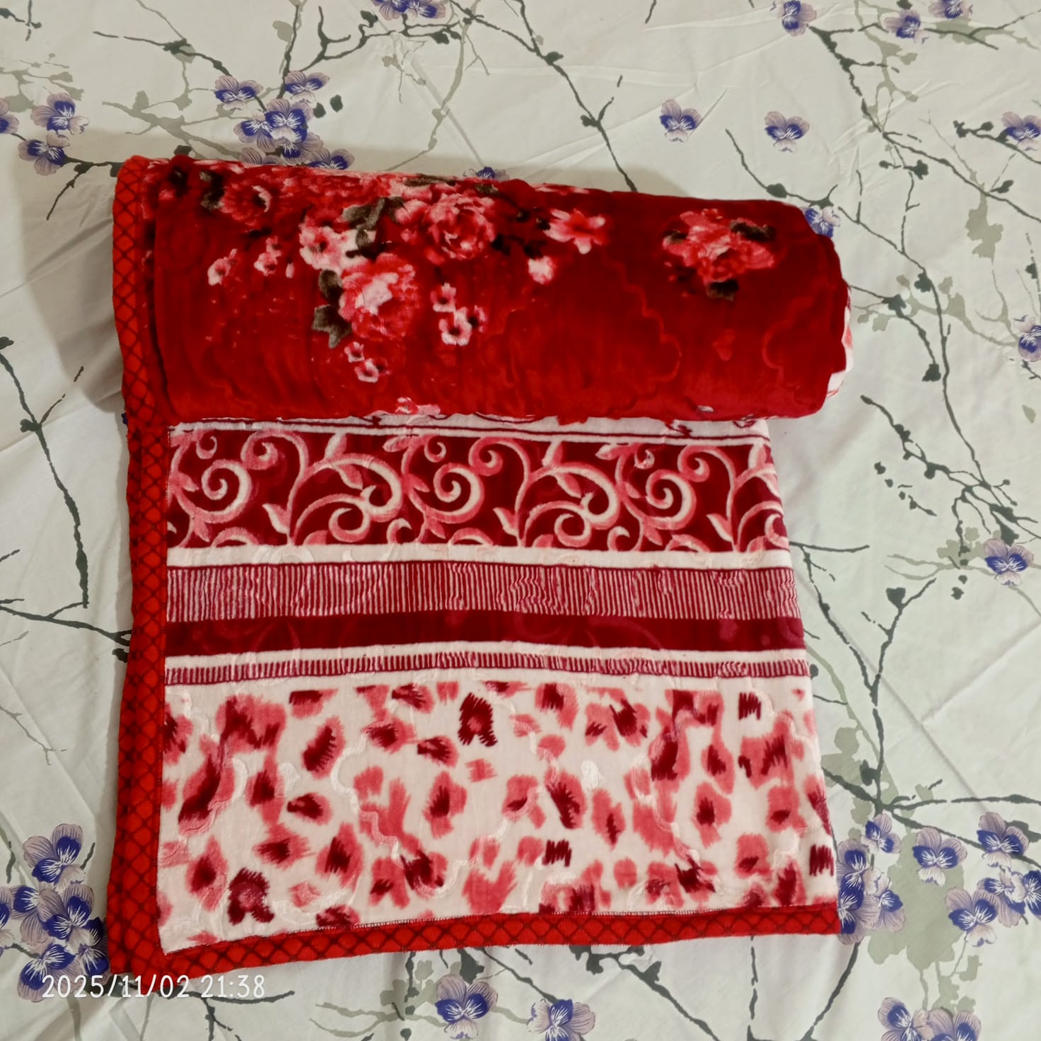 Red floral and patterned blanket on white floral bedsheet