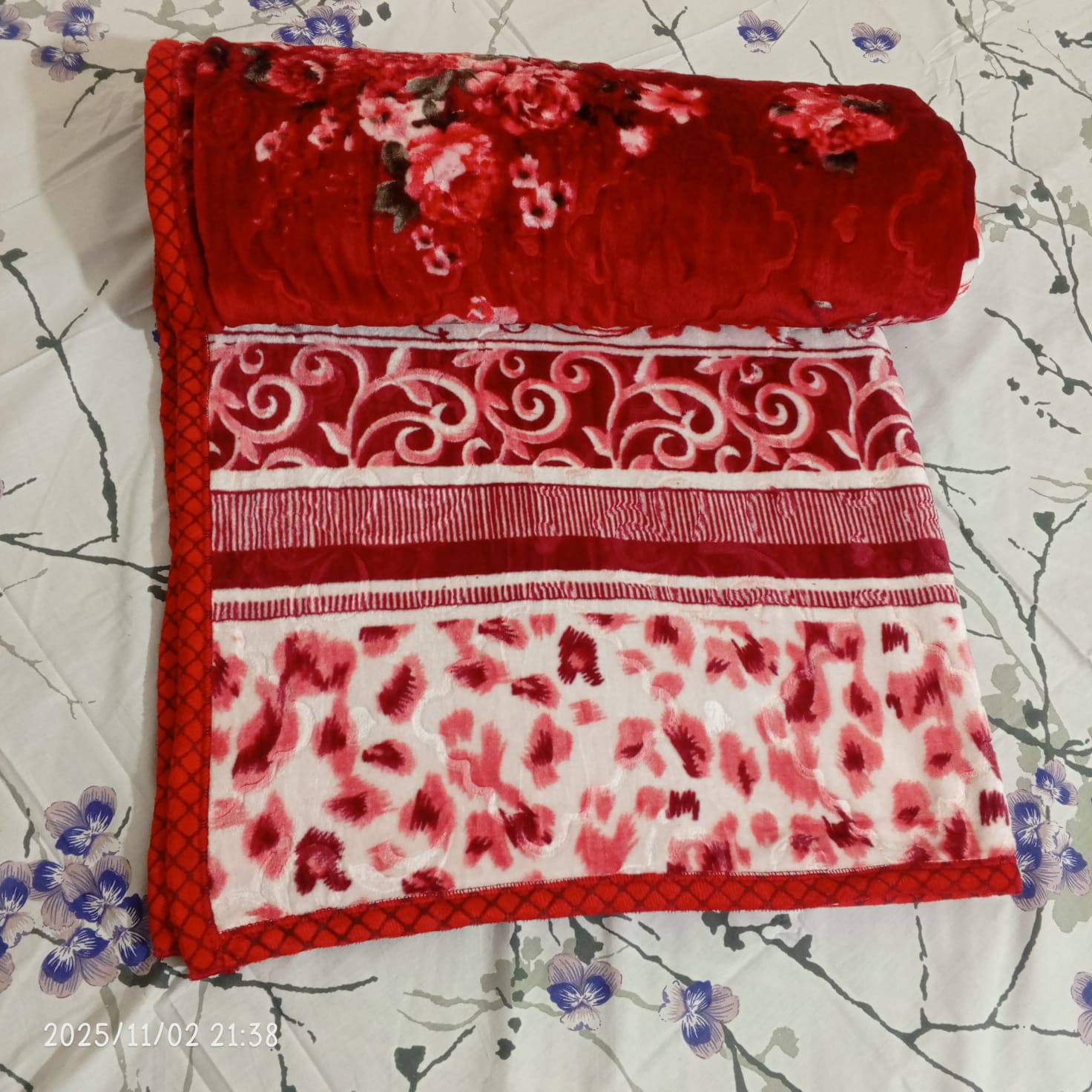 Red and white floral velvet blanket with patterns, displayed on a flower print bedsheet